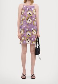 Robe florale lavande avec une coupe droite, des fines bretelles et une texture douce. Associée à un petit sac à main noir et des sandales noires à lanières.