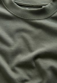 Olīvu zaļš kokvilnas T-krekls ar apaļu kakla izgriezumu, gludu tekstūru un maigu elastību, ar etiķeti apkakles rajonā.