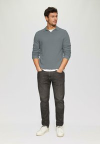 Grauer Waffelstrick-Pullover, weißes Unterhemd, dunkelblaue Jeans und weiße Sneaker. Lässige Passform mit Kragen und gerippten Bündchen.