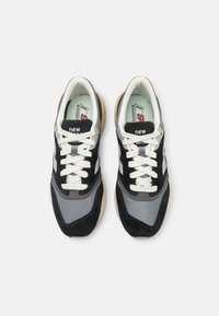 Tenisi negri și gri cu șireturi albe, realizati din materiale de plasă și piele întoarsă, cu tălpi amortizate și un logo pe limbă; design aerodinamic.