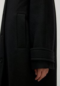 Zwarte wollen jas met gestructureerde afwerking, voorzien van een zijzak, knoopsluiting en opgerolde mouwen. Glad materiaal met een nette silhouet.