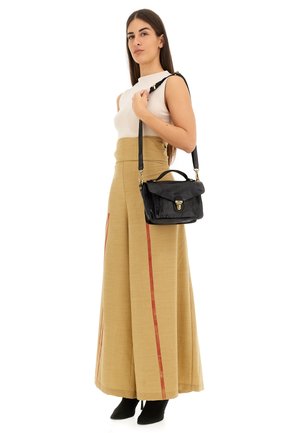 Borsa a tracolla nera in pelle con dettagli in oro, abbinata a pantaloni beige a vita alta e gamba larga con strisce laterali rosse e una maglietta bianca aderente.
