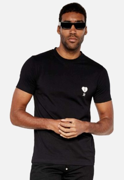 T-shirt nera a maniche corte realizzata in cotone con design aderente. Presenta una piccola grafica di un cuore bianco e dettagli cuciti sul petto.