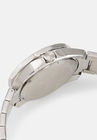 Silberner Edelstahluhren mit rundem Gehäuse, achteckiger Lünette, strukturiertem Krone und Gliederarmband. Die Rückseite zeigt minimalistische Markierungen.