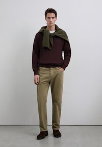 Bordeauxrode trui, olijfgroene sjaal over de schouders gedrapeerd, kaki broek en bruine suède laarzen. Eenvoudig ontwerp, aansluitende pasvorm, zachte textuur.