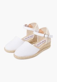 Espadrilles en toile blanche avec une bride de cheville tissée beige et une semelle en jute. Présente un talon plat et un design à bout rond.