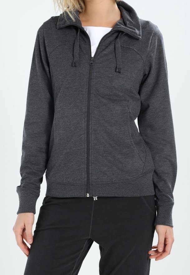 Personne portant un sweat à capuche gris foncé zippé avec cordons et poches avant, associé à un pantalon noir et un tee-shirt blanc à l'intérieur.