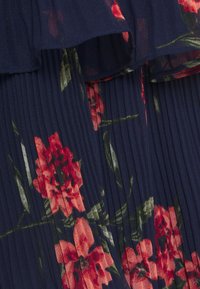 Tissu plissé bleu marine avec un design en couches et un motif floral rouge avec des feuilles vertes.