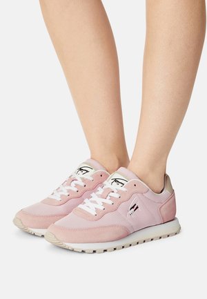 Baskets en mesh rose clair et daim avec lacets blancs portées pieds nus, montrant une vue latérale et de face sur fond blanc.