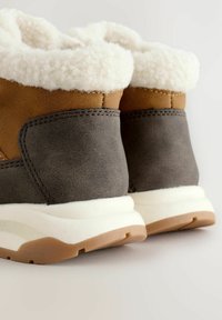 Braune und graue Knöchelstiefel mit weißem Fleecefutter, das eine glatte Textur, eine Gummisohle und gestikte Akzente an den Nähten aufweist.