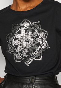 Černé bavlněné tričko s kovově stříbrným mandalovým designem s detailními vzory listů a kruhovými akcenty. Krátké rukávy a kulatý výstřih.