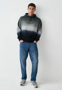 Hanorac cu glugă, având un design gradient de la gri la negru, cu imprimeul "SAN FRAN CALIFORNIA"; asortat cu blugi din denim albastru.