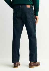 Tume sinised teksad on sirge lõikega, tagataskute ja vööaukudel kaubamärgiga nahast detailidega. Kandmist täiendavad pruunid kingad.