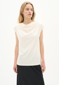 Top à col bénitier et manches courtes en tissu crème doux, avec une coupe décontractée et une texture lisse, associé à une jupe sombre. Détails de design minimalistes.