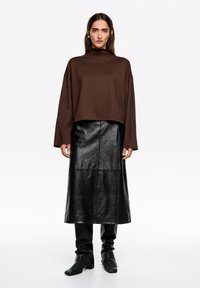 Brązowy krótki top z wysokim dekoltem, zestawiony z czarną skórzaną spódnicą midi oraz czarnymi kozakami za kolano, charakteryzujący się gładkimi fakturami i eleganckim designem.