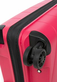 Tvrdý kufr v jasně růžové barvě s texturovaným povrchem. Obsahuje černý zip a robustní dvojitá kola pro snadnou manipulaci.