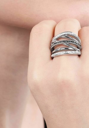 Silberner Multi-Band-Ring mit schwarzen und weißen Steinen, getragen am Mittelfinger einer Hand vor einem hellen Hautton-Hintergrund.