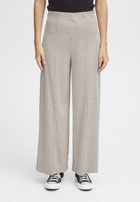Weite Hose in einem hellbeigen Hundszahn-Muster, mit hoher Taille, Falten und einem weichen Material. Kombiniert mit schwarzen Sneakern.
