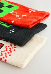 Drei gestickte Socken übereinander gestapelt: leuchtend rot mit grünem Design, schwarz und cremefarben mit roten Mustern. Strukturierter Strick, weiches Gefühl und vielfältige Farben.