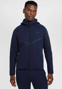 Mornarsko modra Nike jopica z zadrgo in kapuco, ki ima črn poševni poudarek, stranske žepe in eleganten, strukturiran izdelek.