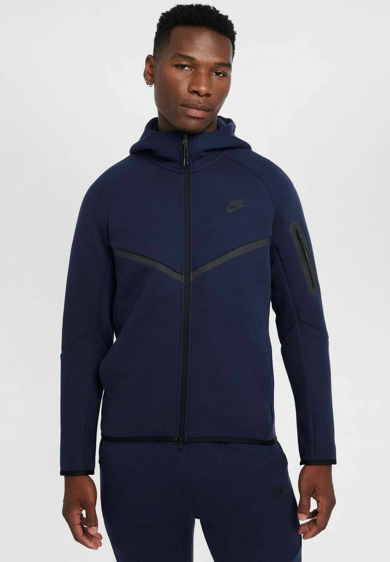 Mornarsko modra Nike jopica z zadrgo in kapuco, ki ima črn poševni poudarek, stranske žepe in eleganten, strukturiran izdelek.