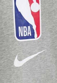 Grå sweatshirt med NBA-logo i blå, rød og hvid, med stort hvidt Nike-swoosh-logo nedenfor. Stoffet har et blødt, struktureret udseende.