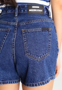 Shorts de mezclilla en azul oscuro, con una cintura alta, costuras visibles y dos bolsillos traseros. Etiqueta de la marca en la cintura con detalles de texto.