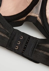 Čierne zapínanie podprsenky na chrbte so tromi háčikmi a béžovým vnútorným lemom, ktoré ukazuje textúru látky a detaily šitia.