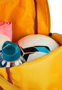 Mochila amarilla abierta que revela una pelota de fútbol blanca con acentos negros y azules, una botella de agua azul y una toalla rosa en su interior.