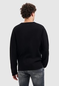 Schwarzer Pullover mit Rundhalsausschnitt und langen Ärmeln, der eine glatte Textur aufweist. Kombiniert mit hellgrauen, ausgewaschenen Jeans.