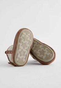 Braune Wildlederschuhe mit flacher Sohle und einem Sternmuster. Die Seiten sind hellbeige und haben eine weiche Textur. Größe 6 ist auf der Sohle sichtbar.