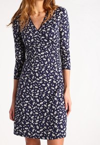 Marinblå klänning med blommönster, trekvartsärmar, V-ringning och figurnära midja. Tillverkad av mjuk, lätt tyg med en slät textur.