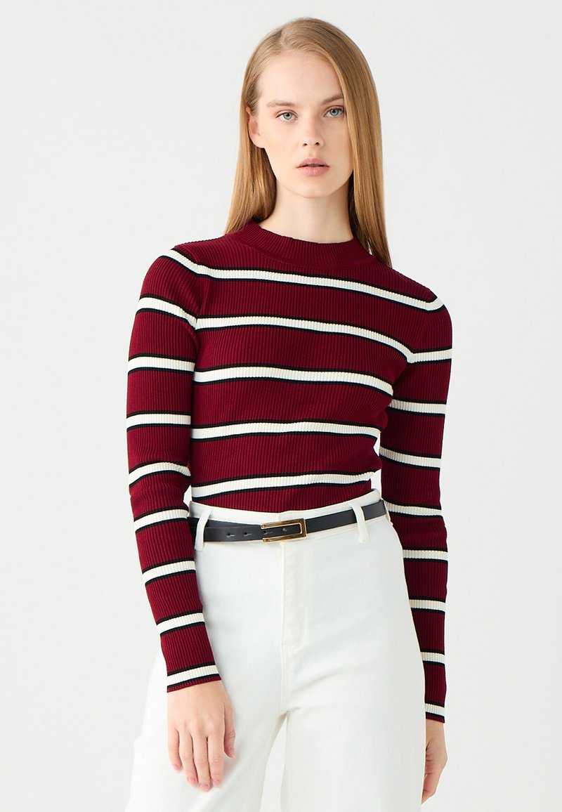 Maglietta a maniche lunghe a coste color mogano con strisce orizzontali bianche e nere; design aderente, scollatura rotonda, abbinata a pantaloni bianchi e cintura nera.