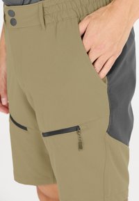 Khakifärgade shorts med en svart sidopanel, elastisk midja och två dragkedjefickor. Slät textur och lätt material.