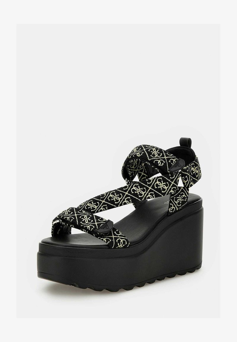 Svart plattformssandal med flätade remmar som har ett geometriskt mönster i guld. Texturerad sula ger grepp; solid, upphöjd klack för höjd.