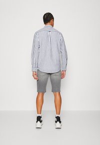 Koszula w paski z guzikami w kolorze niebieskim i białym, zestawiona z szarymi szortami jeansowymi. Dopełnieniem są czarno-białe trampki za kostkę.