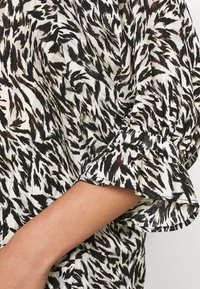 Schwarz-weiße gemusterte Bluse mit lockerem Schnitt, weichem, leichtem Stoff und ausgestellten Ärmeln mit Rüschensaum.