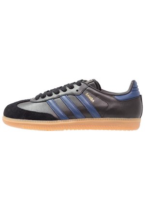 Sort og blå Adidas Samba sneaker med gummisål, sorte snørebånd, ruskindståhætte og gyldent "SAMBA" mærke på siden.