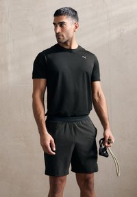 Svart treningstrøye med ribbestruktur, kombinert med mørke shorts. Personen holder et hoppetau, og viser frem design og funksjonalitet i treningstøy.