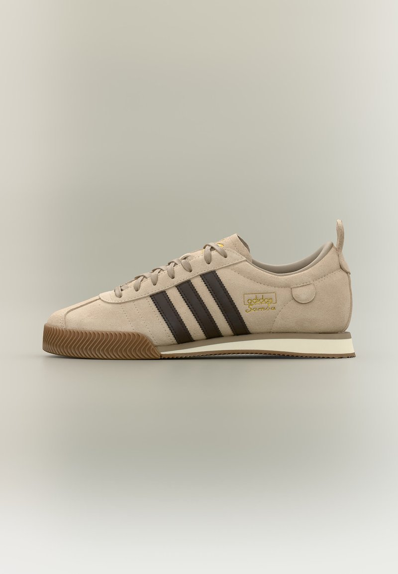 Baskets Adidas Samba beige avec des bandes marron foncé, semelle en gomme, matière en suède et détails du logo doré sur le côté.