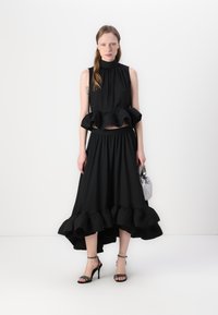 Ensemble noir deux pièces comprenant un haut sans manches avec un ourlet volé et une jupe assortie avec une taille et un ourlet volés. Les accessoires incluent un sac argenté.