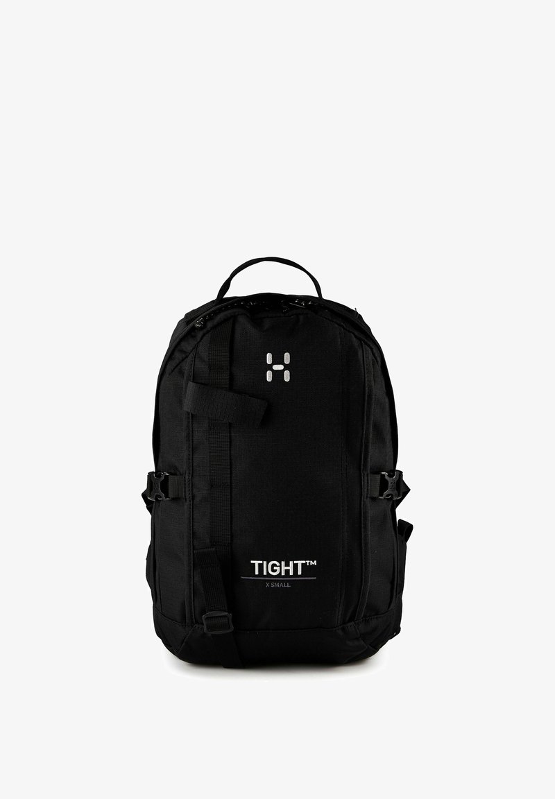 Sac à dos compact noir avec sangle frontale, boucles latérales, poignée supérieure et texte "TIGHT™ X SMALL" sur le panneau avant inférieur.