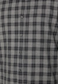 Camisa de botones de cuadros grises con un patrón a cuadros y acentos negros, textura suave y botones decorativos en la parte delantera.