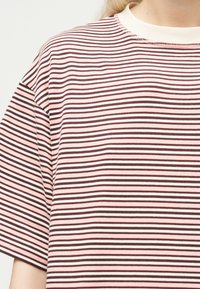 Κοντινή λήψη ενός ατόμου που φοράει ριγέ κοντομάνικο πουκάμισο με οριζόντιες ρίγες σε ροζ, άσπρο και καφέ χρώμα, με λευκό γύρο γιακά.