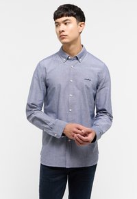 Jasnoniebieska koszula z długim rękawem, z kołnierzykiem i białymi guzikami. Posiada subtelną teksturę oraz małe haftowane logo na piersi.