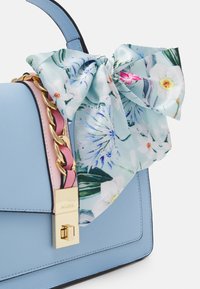 Niebieska syntetyczna torebka z kwiecistym jedwabnym szalikiem przewiązanym jako akcent, złotym łańcuszkiem i złotym zamkiem na boku.