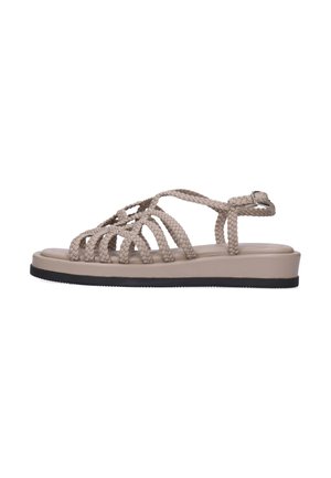 Beige flad sandal med flettede remme, ankelspænde og sort sål, vist i sideprofil på hvid baggrund.