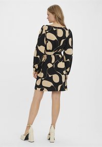 Black dress with beige abstract pattern, long sleeves, a belted waist, and a knee-length hem. Paired with chunky heeled shoes.