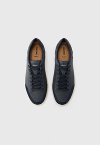 Baskets bleu marine avec une surface lisse et texturée, dotées d'un design à lacets, d'une semelle en caoutchouc contrastante de couleur fauve, et de semelles intérieures brandées.