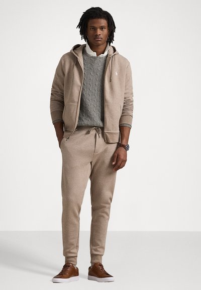 Beige hoodie with front pockets, paired with a gray cable-knit sweater and matching sweatpants. Brown sneakers complete the outfit.